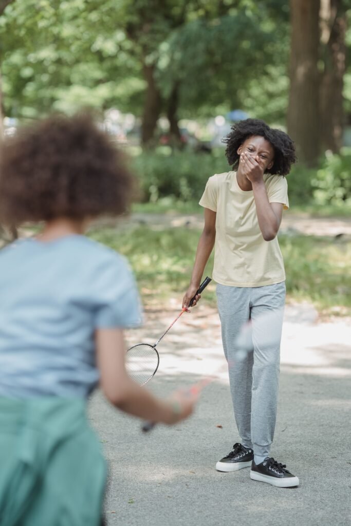 Two girls joyfully playing badminton outdoors, sharing laughter on a sunny day.