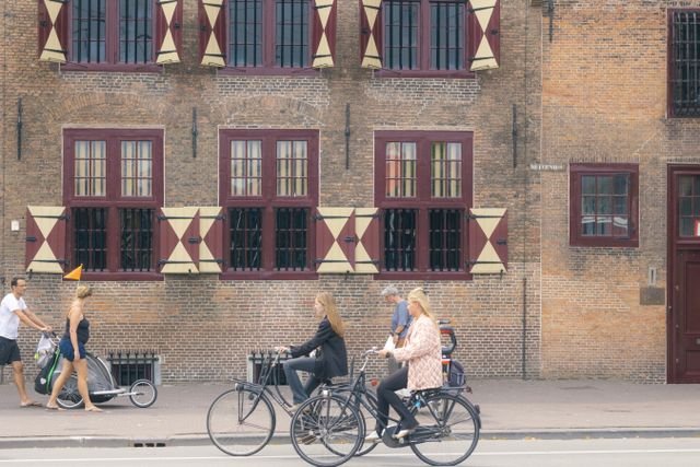 People cycling and walking by a historic building with unique shutters on a city street.
