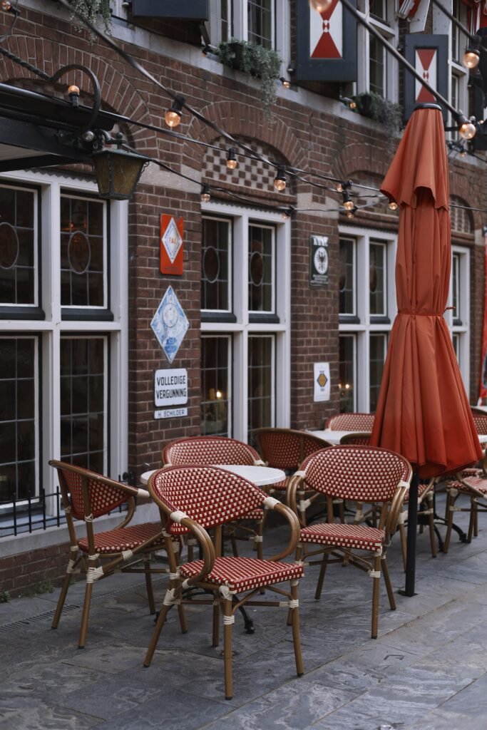 Charming Dutch café with vintage decor, outdoor seating, and a red umbrella in Amsterdam, Netherlands.