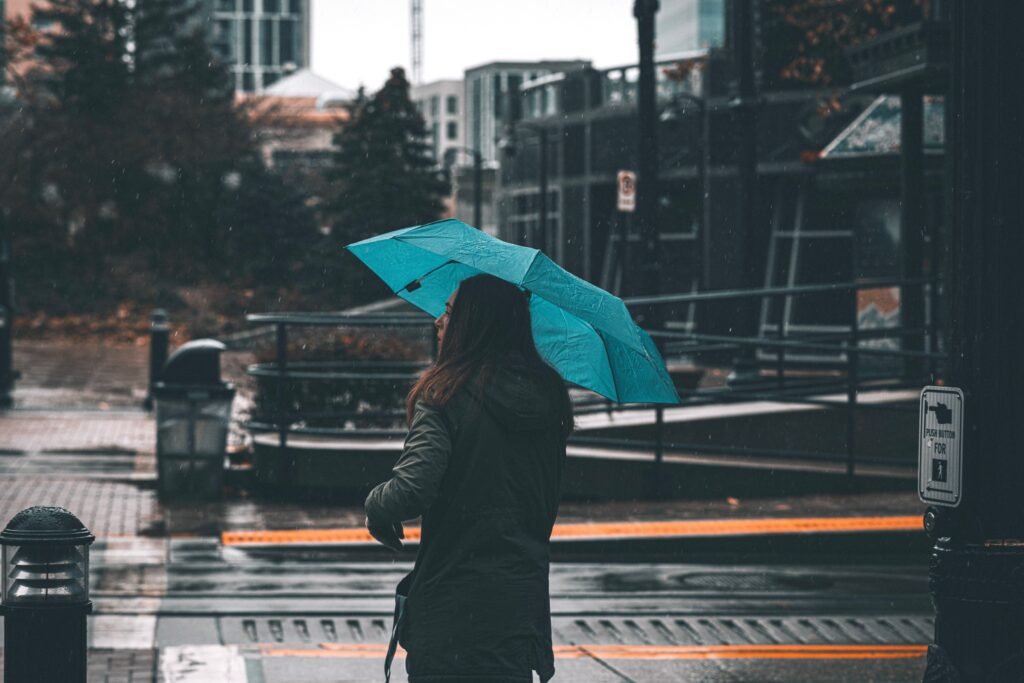 A woman with a blue umbrella walks through a city street on a rainy day, capturing the essence of urban life.